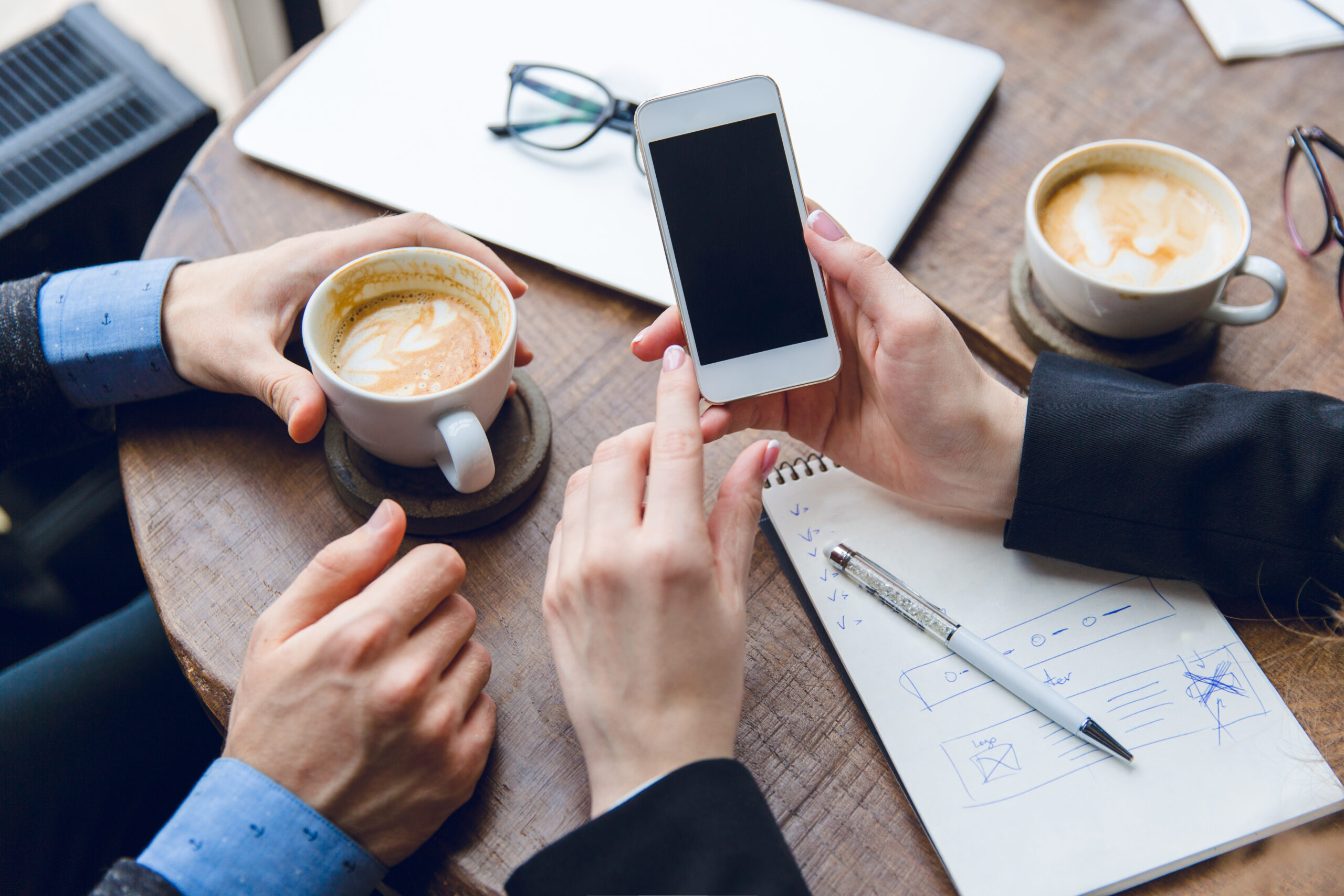 close-up-white-smartphone-woman-s-hands-two-colleagues-sitting-coffee-table-drinking-coffee